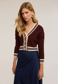 Cardigan bordeaux con un motivo a maglia testurizzata, scollo a V e strisce crema. Presenta sei bottoni frontalmente e maniche a tre quarti.