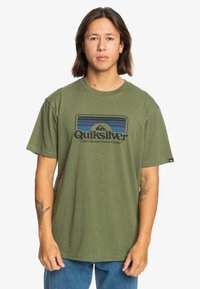 Olive green cotton T-shirt with a crew neck, short sleeves, and a graphic logo design in blue and black featuring mountains and text.