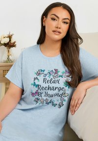 Ljusblå bomull t-shirt med korta ärmar, med ett fjärils mönster och texten "Slappna av, ladda om och koppla av" i ett dekorativt typsnitt.