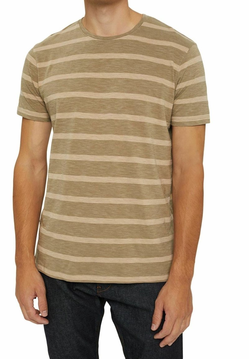 Adulte portant un t-shirt à manches courtes rayé horizontal beige et marron clair, et un jean bleu foncé, debout avec les bras détendus le long du corps.