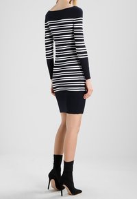 Abito a righe blu navy e bianche, a coste, con maniche lunghe, scollo off-the-shoulder, silhouette aderente e lunghezza sopra il ginocchio.