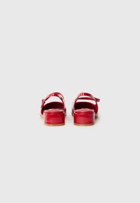 Røde patentlær sandaler med en blank finish, der har en bred rem, justerbar ankelspænde og en blokhæl. Bagudblik.