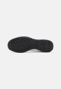 Semelle extérieure en caoutchouc noir avec une texture antidérapante, présentant un motif en zigzag et des formes arrondies. Semelle intermédiaire blanche avec une légère courbure, au design minimaliste.