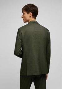 Veste de costume ajustée vert foncé, en tissu texturé, fente simple au dos, revers crantés et manches longues avec accents de boutons.
