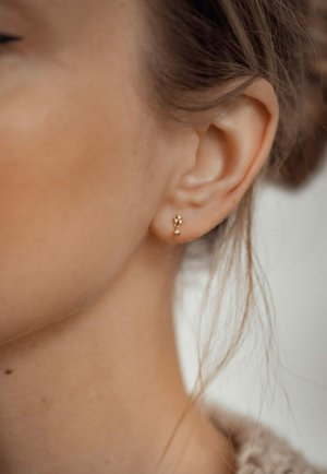 Goldene Ohrstecker mit floralem Design, das mit kleinen klaren Steinen verziert ist. Die Ohrringe sind schlicht und dezent und betonen die natürliche Kurve des Ohrs.