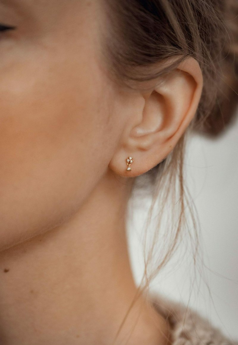Gouden studs met een bloemenontwerp, versierd met kleine heldere stenen. De oorbellen zijn eenvoudig en discreet, en benadrukken de natuurlijke kromming van het oor.