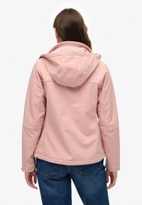 Chaqueta softshell rosa con capucha, que presenta una textura suave, bolsillos laterales y un diseño ligeramente entallado en la cintura.