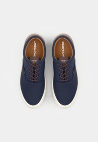 Navy canvas sneakers with brown laces, rounded toe, contrasting white rubber sole, and branded insoles, featuring a simple design.