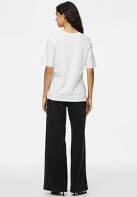 Hvid kortærmet t-shirt med rund halsudskæring, parret med høj talje sorte, brede bukser. T-shirten har sideslidser.