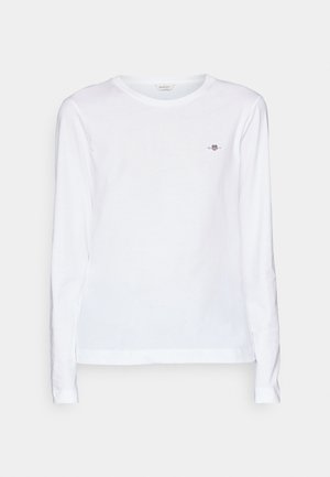 Valkoinen pitkähihainen T-paita, jossa on pyöreä kaula-aukko, valmistettu pehmeästä puuvillasta. Paidassa on pieni brodeerattu logo rintamuksessa ja hihansuissa.