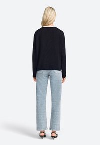 Maglione nero in maglia con un fit rilassato, abbinato a jeans azzurri chiari a fantasia. I jeans hanno un orlo sfilacciato e tasche posteriori oblique.