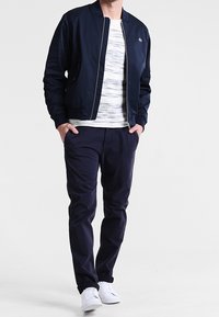 Granatowa bombka ze ściągaczem, biała koszulka w paski i ciemne spodnie. Białe sneakersy dopełniają stylizację. Prosty design, swobodny krój.