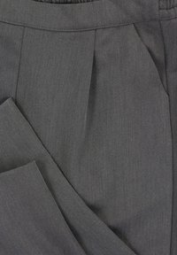Op maat gemaakte grijze broek van textuurstof, met een geplooide voorkant en een gladde tailleband. De stof heeft een subtiel diagonaal patroon.