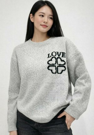 Femme aux longs cheveux noirs portant un pull gris avec le mot "LOVE" et quatre formes de cœur noires sur la poitrine.