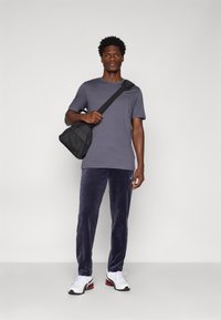 Γκρίζο κοντομάνικο μπλουζάκι με στρογγυλή λαιμόκοψη, συνδυασμένο με άνετες ναυτικές φόρμες. Μαύρη τσάντα χιαστί και άσπρα αθλητικά παπούτσια με κόκκινες λεπτομέρειες.