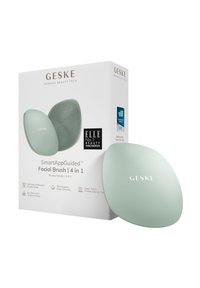 Brosse faciale avec une surface en silicone douce dans une teinte vert menthe, dotée d'un design ergonomique. L'emballage comprend des détails sur le produit et des récompenses.