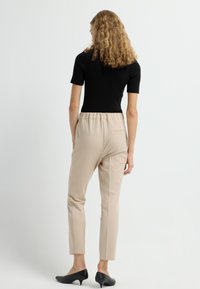 Zwarte geribbelde korte mouwen top gecombineerd met beige tapered trousers en zwarte puntige hakken. Gladde textuur en details van de elastische tailleband zichtbaar.