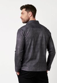 Donkergrijze button-up blouse met subtiele textuur, lange mouwen en een klassieke kraag. Een casual ontwerp met een accent op de achterzak.