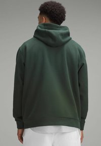 Donkergroene hoodie van zacht materiaal. Heeft een grote capuchon en boorden aan de mouwen. De achterkant heeft een gladde afwerking zonder versieringen.