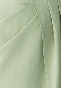 Svijetlozelena tkanina glatke teksture, s naboranim dijelovima i kontrastnim šavovima duž šavova.