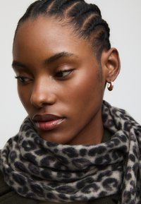 Sciarpa con stampa leopardata realizzata in tessuto morbido, con sfumature di grigio e nero; indossata morbida intorno al collo, con trama liscia e caduta fluida.