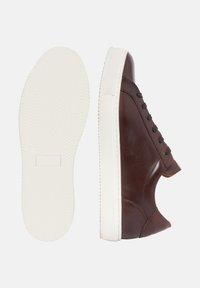 Brauner Ledersneaker mit einer weißen Gummisohle, ausgestattet mit einer glatten Oberfläche, runder Zehenpartie und sechs schwarzen Ösen für die Schnürung.