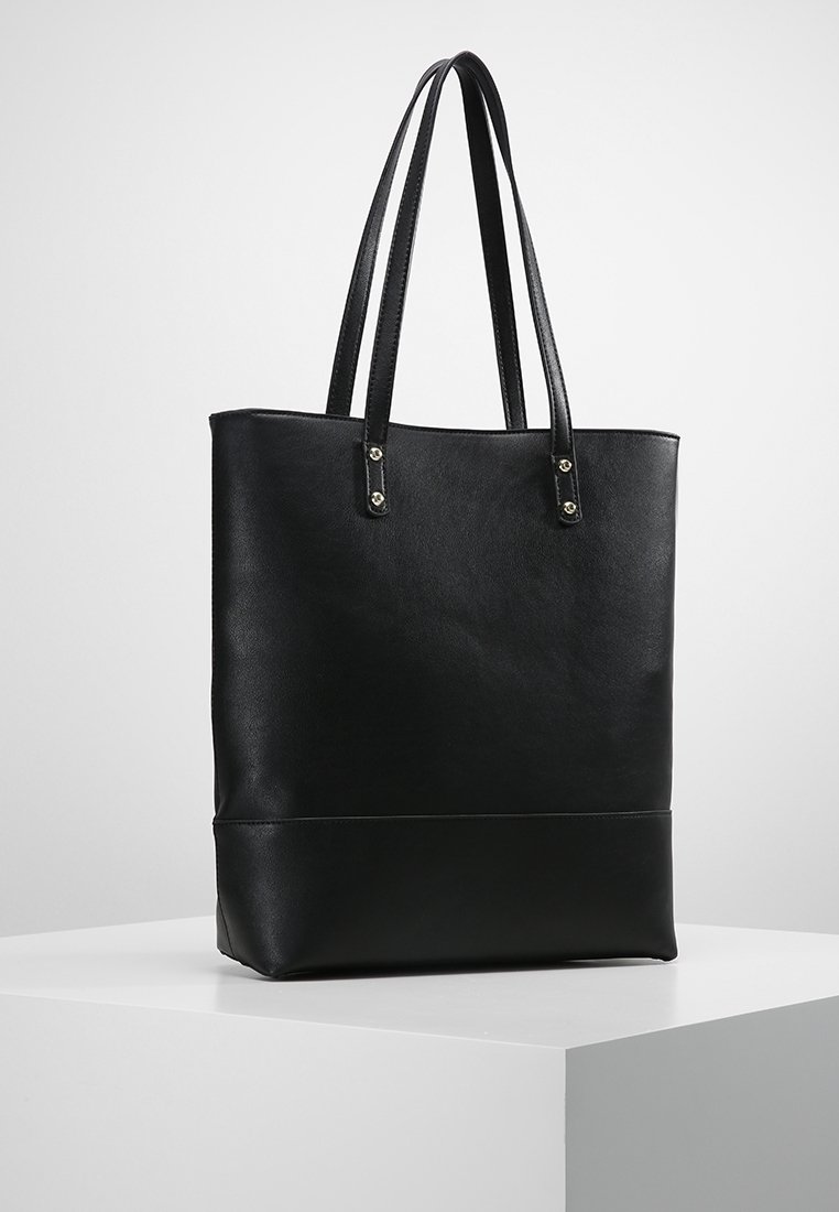 Sac cabas en cuir noir avec longues doubles anses, forme rectangulaire et design minimaliste sur un piédestal blanc sur fond gris clair.