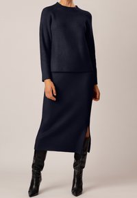 Granatowy prążkowany zestaw swetra i midi spódnicy z bocznym rozcięciem. Długie rękawy, dekolt typu crew oraz dopasowana sylwetka. Połączony z czarnymi kozakami za kolano.