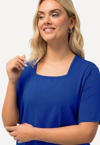 Top de manga corta azul real con escote cuadrado, hecho de un tejido suave y liso; cuenta con costuras limpias y un ajuste relajado.