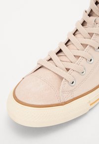Világos rózsaszín vászon sneaker velúr díszítéssel, kerek orral, bézs gumitalppal és lapos fűzőkkel, amelyek ezüst fűzőlyukakon át vannak fűzve.