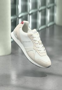 Λευκό και μπεζ αθλητικό παπούτσι με υφασμάτινη υφή και δερμάτινες λεπτομέρειες, που διαθέτει ταμπελάκι με λογότυπο και κόκκινη λεπτομέρεια στη φτέρνα. Ελαφρύς καουτσούκ πάτος.