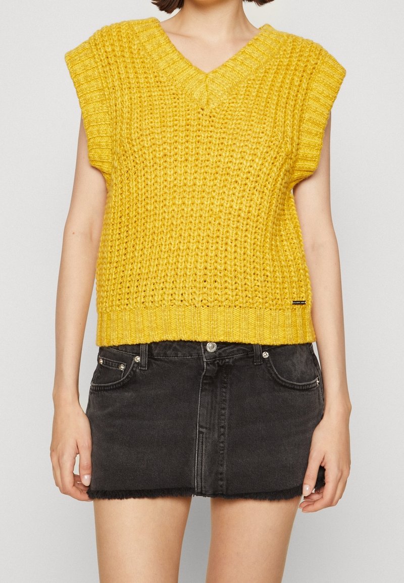 Geel gebreid mouwloos topje met een V-hals, voorzien van een textuurpatroon en een geribbelde zoom, gecombineerd met een zwarte denim mini rok.