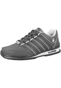 Grauer Sportschuh mit glattem synthetischem Obermaterial, weißen und grauen gestreiften Akzenten, runder Zehenpartie und gepolstertem Sohlen. Branding auf der Seite sichtbar.