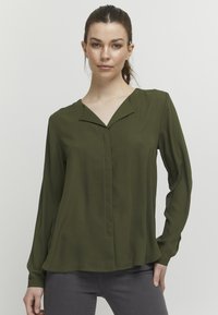 Olive green long-sleeve blouse with a V-neck, featuring a subtle front seam and smooth texture. Lightweight fabric with a relaxed fit.