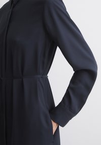 Abito blu navy con maniche lunghe, corpino strutturato, cintura in vita e tessuto morbido. Presenta un colletto classico e pieghe sottili all'orlo.