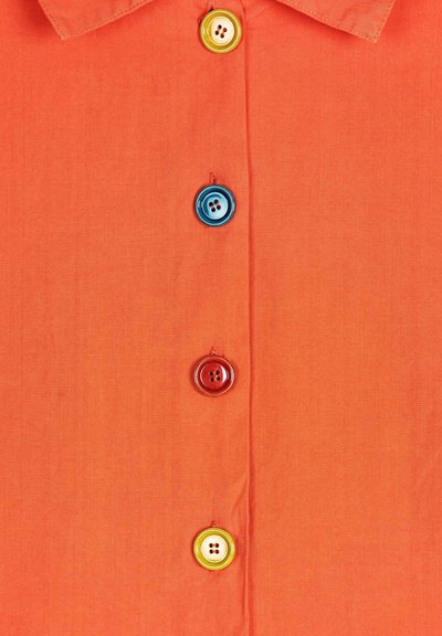 Oranssi paita, jossa on sileä pinta, ja viisi moniväristä nappia: sininen, punainen, keltainen ja kaksi valkoista, joissa kummassakin on neljä reikää.