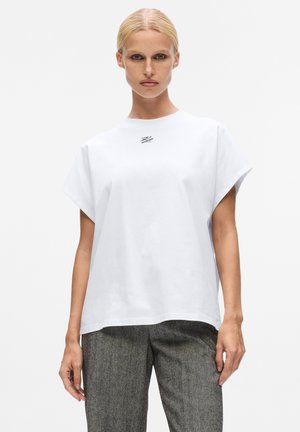 Oversized weißes T-Shirt aus Baumwolle, mit Rundhalsausschnitt und kurzen Ärmeln, versehen mit einem kleinen schwarzen Logo auf der Brust.