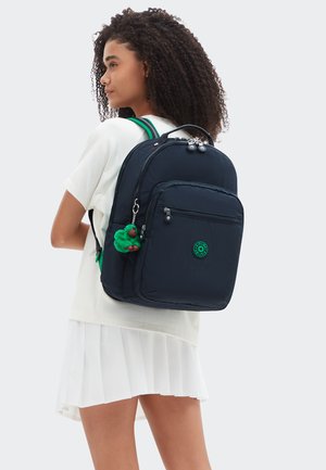 Sac à dos bleu marine à finition texturée, avec une poche frontale zippée, un logo vert et un accessoire porte-clés vert suspendu. Bretelles ajustables.