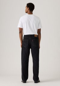 Zwart denim jeans met een rechte pasvorm en twee achterzakken. Gecombineerd met een plain wit T-shirt. Lederen merkpatch zichtbaar op de tailleband.