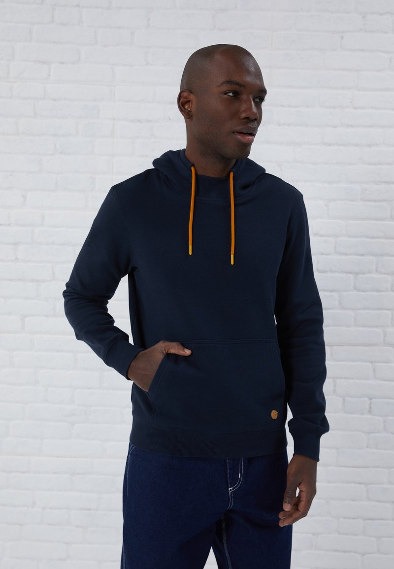Sudadera de marina hecha de una tela suave, con cordones naranjas, un bolsillo frontal y un parche de logo redondo en el dobladillo. Diseño de corte casual.