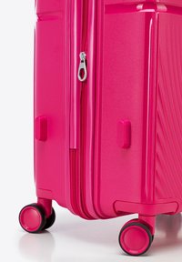 Světlé růžové tvrdé kufřík s texturovaným povrchem, dvojitými zipy a čtyřmi černými kolečky pro snadnou mobilitu.