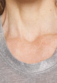 Tejido de suéter gris de punto con un escote redondeado, que presenta un sutil brillo. Textura suave y ligero acanalado a lo largo del cuello.
