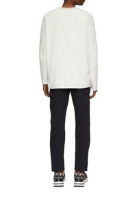 Langsleeve, crewneck shirt in lichtgrijze katoen. Gepaard met zwarte cargobroeken met zijzakken en zwarte sneakers met witte accenten.