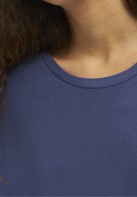 Maglietta blu navy con scollatura rotonda, realizzata in un tessuto morbido, caratterizzata da una texture liscia e un design essenziale. Inquadratura ravvicinata della parte superiore del torso.