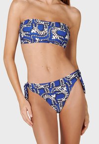 Plavi bandeau bikini s bijelim apstraktnim uzorcima. Gornji dio je bez naramenica, a donji dio ima detalje s vezanjem sa strane. Cijeli bikini ima glatku teksturu.