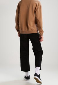 Brun bomullströja med ribbade ärmslut, kombinerad med svarta manchesterbyxor med vida ben. Vita strumpor och svarta sneakers avslutar outfiten.