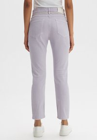 Jeans in denim lilla con una vestibilità dritta, caratterizzati da un alto punto vita, due tasche posteriori e un passante per cintura bianco. Abbinati a sneakers bianche.