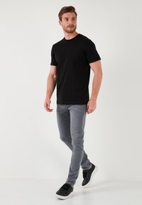 Camiseta de algodón negra, de manga corta, con cuello redondo; combinada con jeans ajustados de color gris claro y zapatillas negras con suela blanca y tiras de velcro.