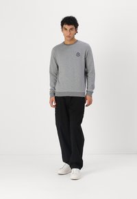 Hanorac gri cu guler rotund, cu un logo mic pe piept, asociat cu pantaloni negri și adidași albi. Design simplu, casual.