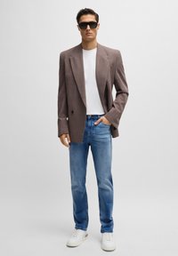 Brązowa dwurzędowa marynarka, biała koszulka, jasnoniebieskie dżinsy i białe trampki. Dodatki obejmują czarne okulary przeciwsłoneczne.